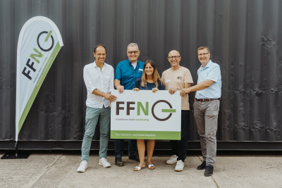 Gruppe von fünf Menschen steht lachend vor einer Wand und hält ein Plakat mit Logo FFN vor sich.
