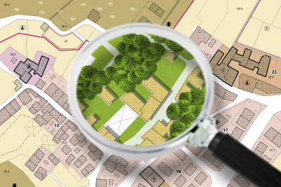 Imaginärer Stadtplan mit Gebäuden und Straßen. eine Lupe unter der man die Stadt mit grüner Bepflanzung sieht